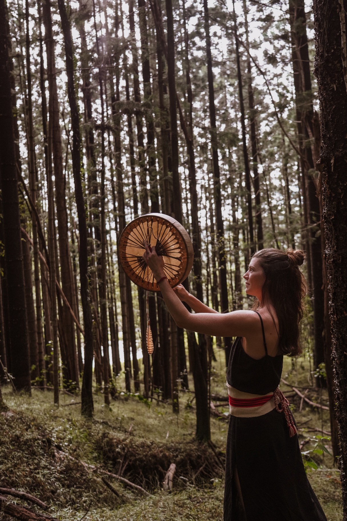Rebecca Furnell holding a hand drum in a sunlit forest